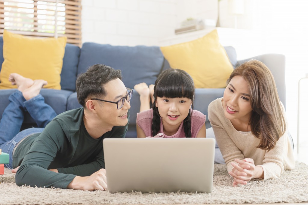 Happy Asian family using computer laptop together on sofa at home living room.