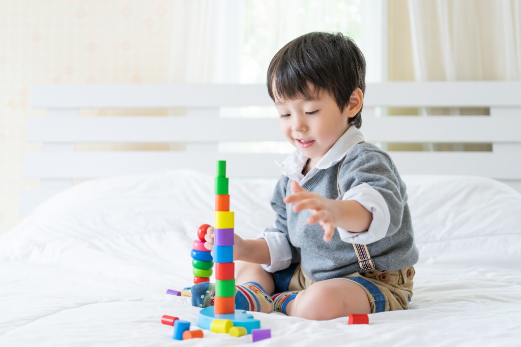 Asian cute boy sitting on bed and joyful with colorful wooden learning toy in the bedroom, copy space